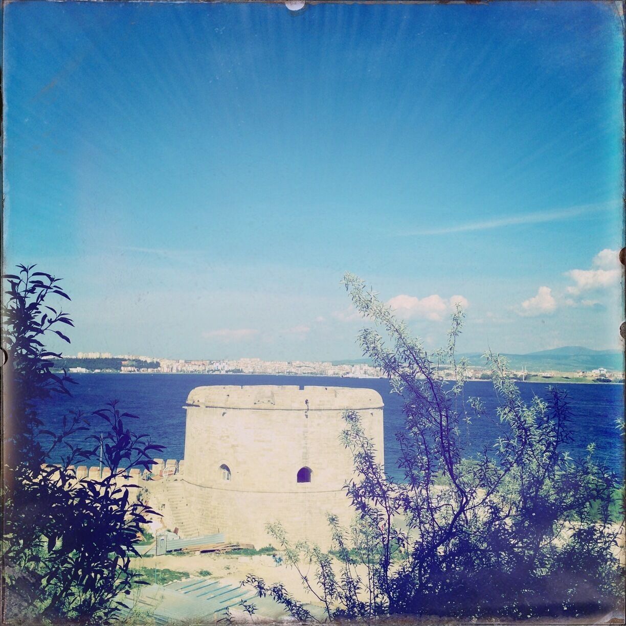 A coastal fortification with a clear view of the sea and a distant city skyline.