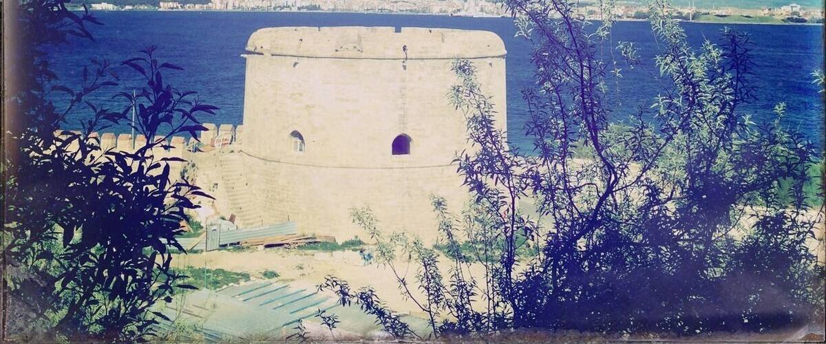 A coastal fortification with a clear view of the sea and a distant city skyline.