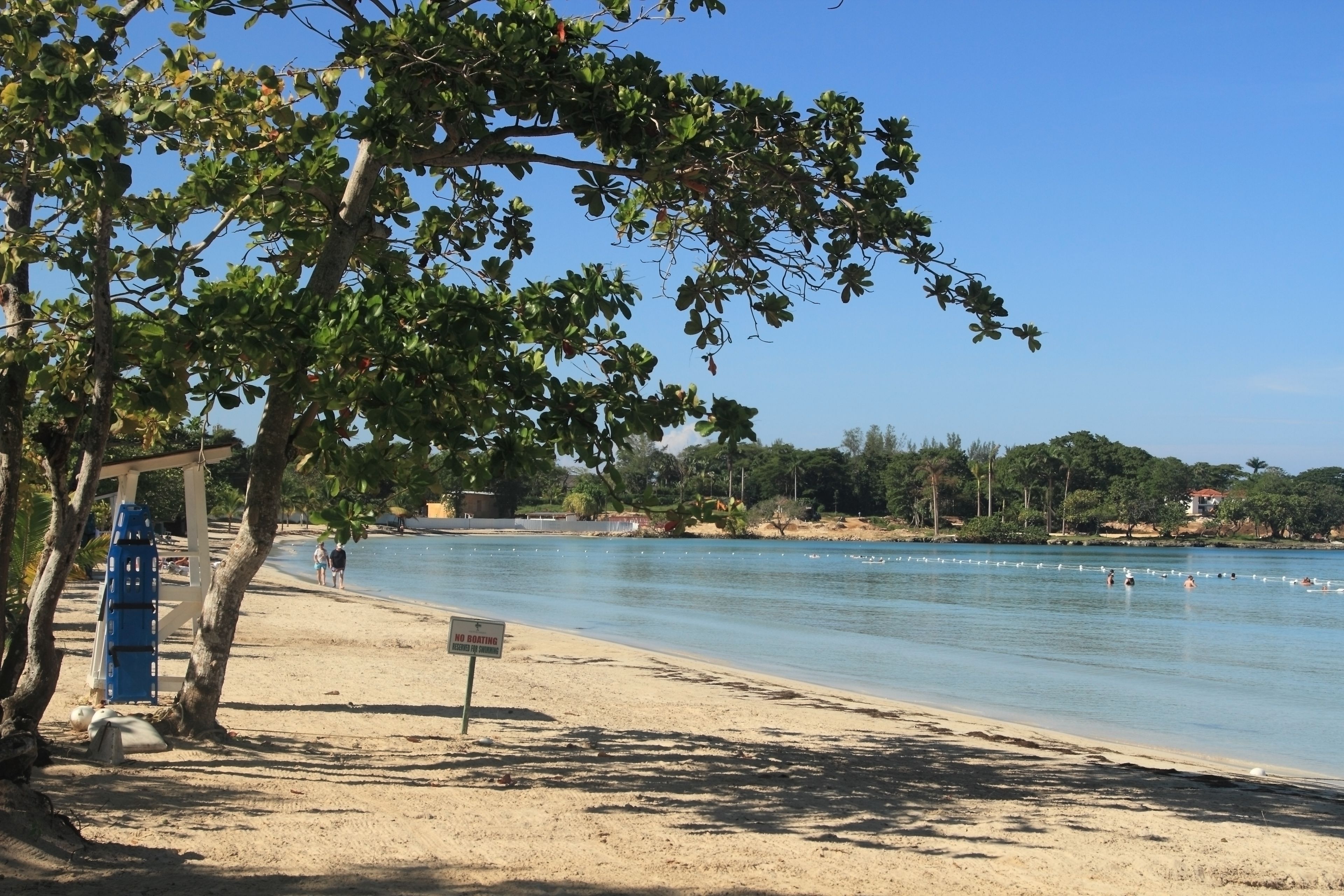 A beach with clear blue water, a no boating sign, and a row of trees.