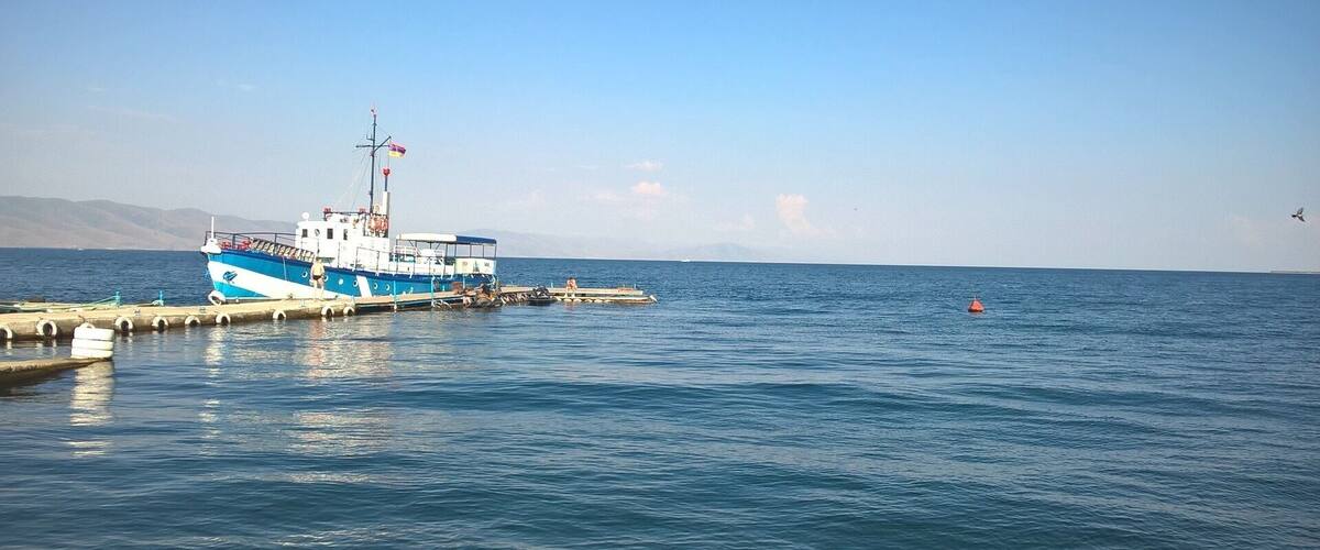 A blue and white boat docked at a pier with calm water and a clear sky.