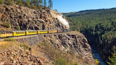 A yellow train on a steep mountain track with a river below.