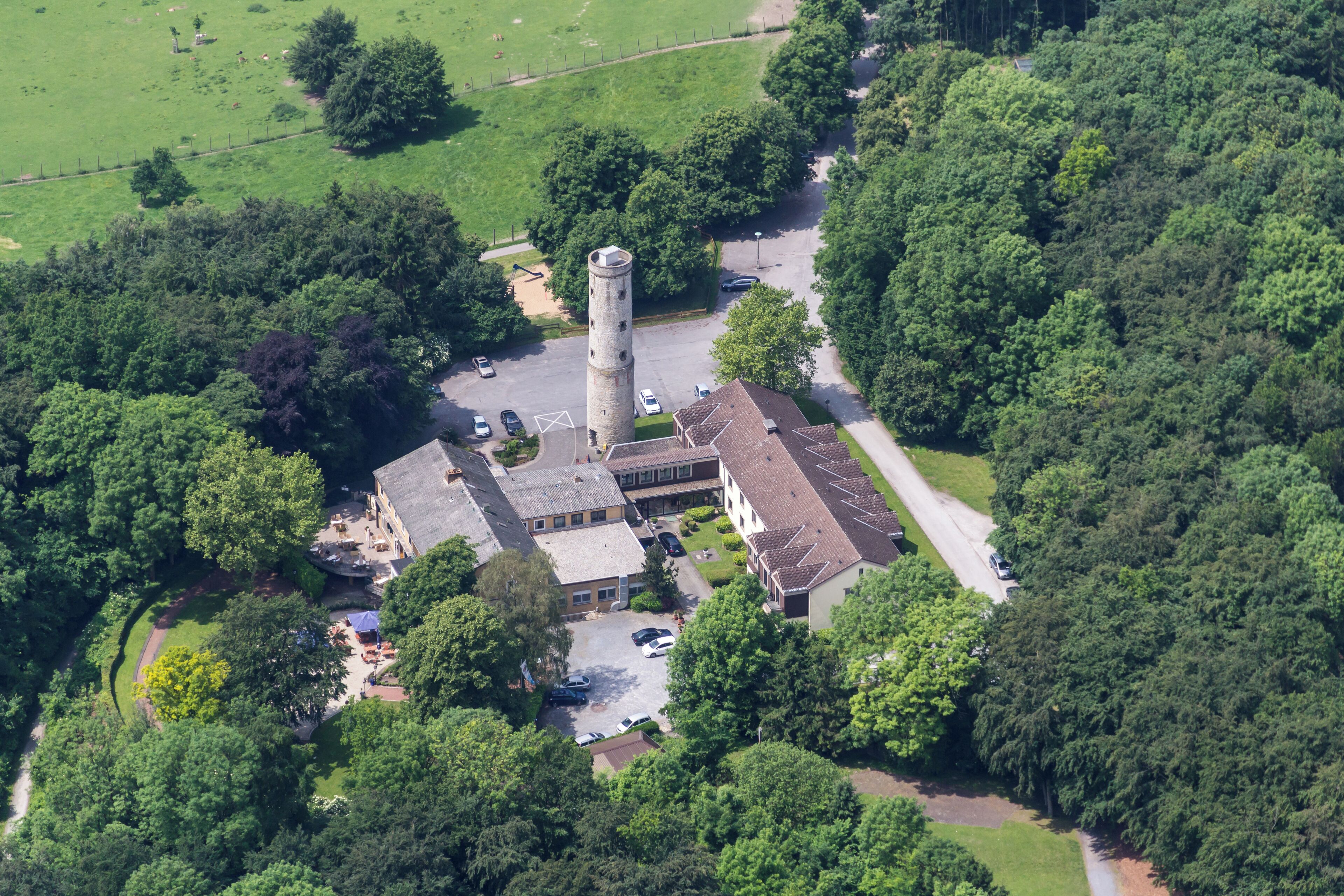An aerial view of a historic building with a tower, surrounded by lush greenery and a parking area.