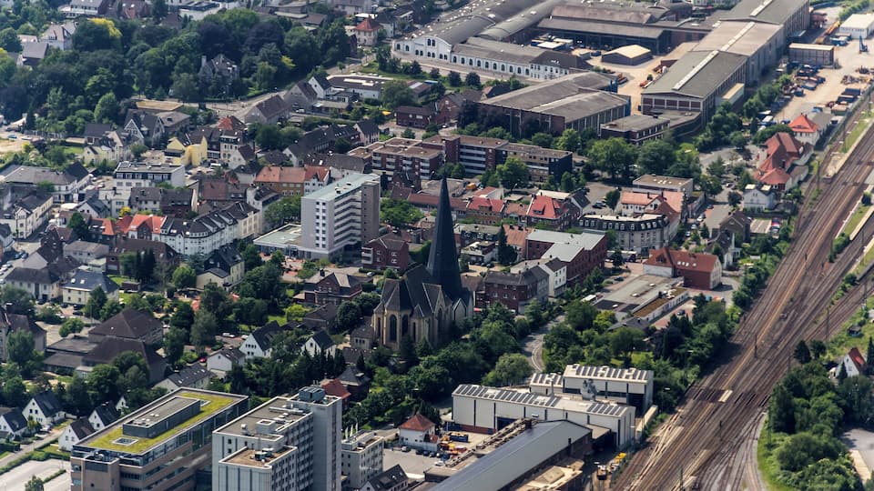 An aerial view of a city with dense housing, a prominent church, and railway tracks.