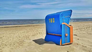 A blue beach chair with the number 180 on it, positioned on a sandy beach with the ocean in the background.