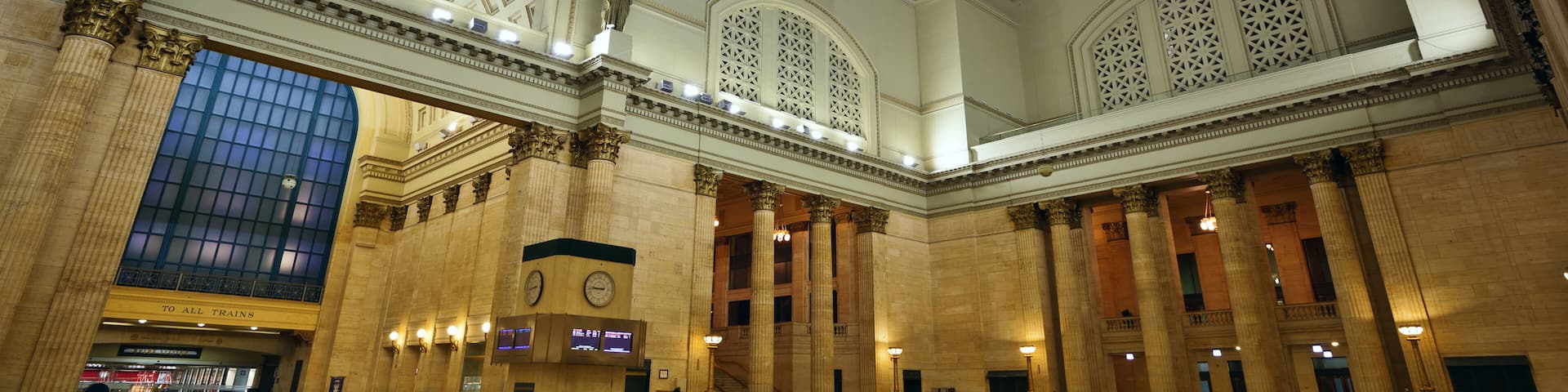 A grand train station with a large glass dome, ornate columns, and a spacious interior.