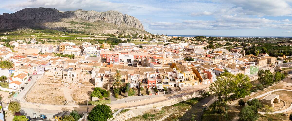 A coastal town with a prominent mountain in the background, a river, and a mix of traditional and modern architecture.
