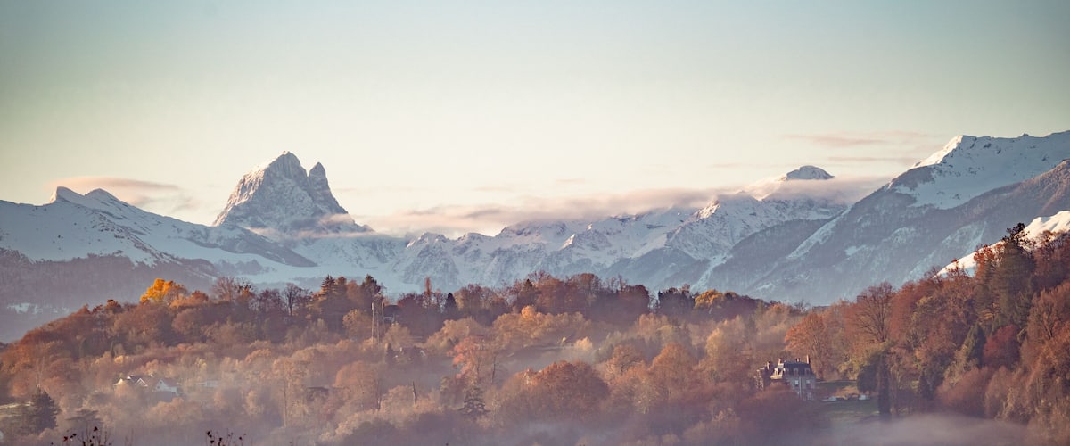 A mountainous landscape with snow-capped peaks, autumn-colored trees, and a misty valley.