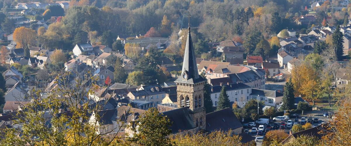 A town with a prominent church tower, surrounded by autumn-colored trees and residential buildings.