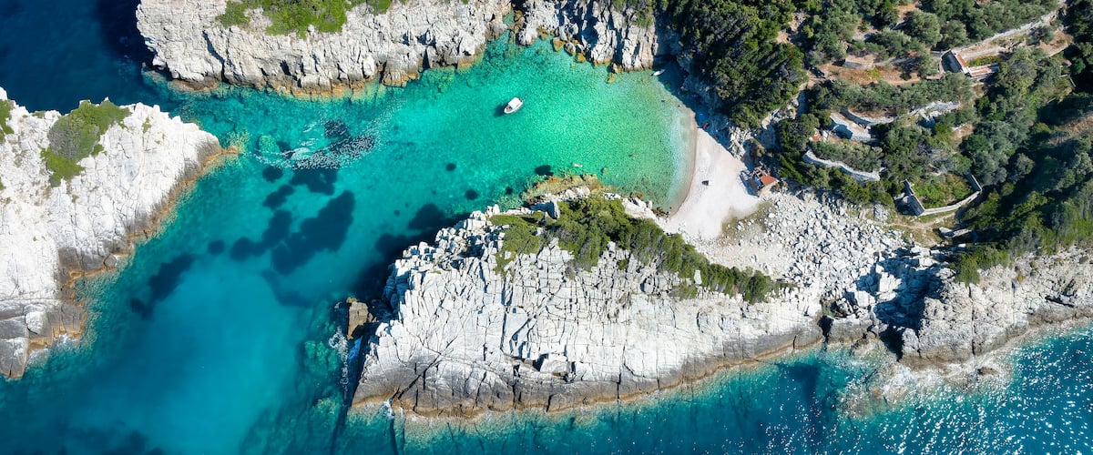 A coastal landscape with rocky cliffs, clear turquoise waters, and dense greenery.