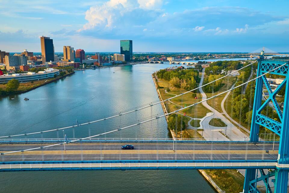 Un puente colgante sobre un río, con un paisaje urbano al fondo.
