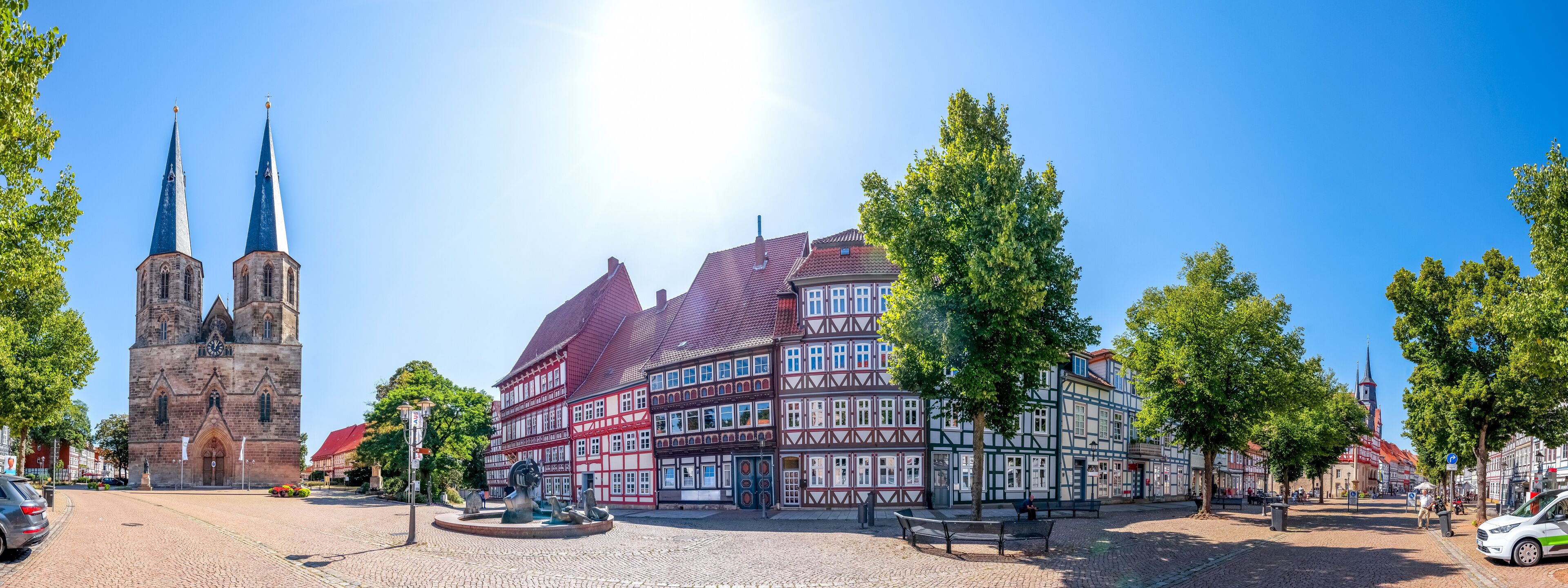 A cobblestone square with a church, traditional half-timbered buildings, and a clear blue sky.