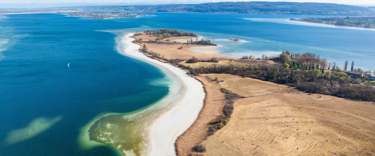 Un paisaje costero con una playa de arena, un mar azul cristalino y colinas ondulantes al fondo.
