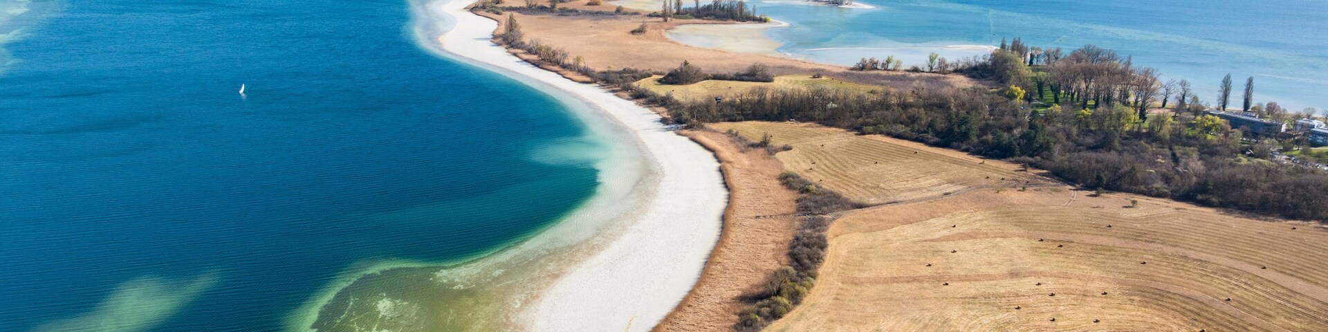 Un paisaje costero con una playa de arena, un mar azul cristalino y colinas ondulantes al fondo.
