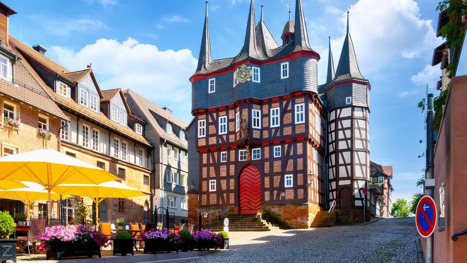A historic European town square with cobblestone streets, traditional half-timbered buildings, and a prominent clock tower.
