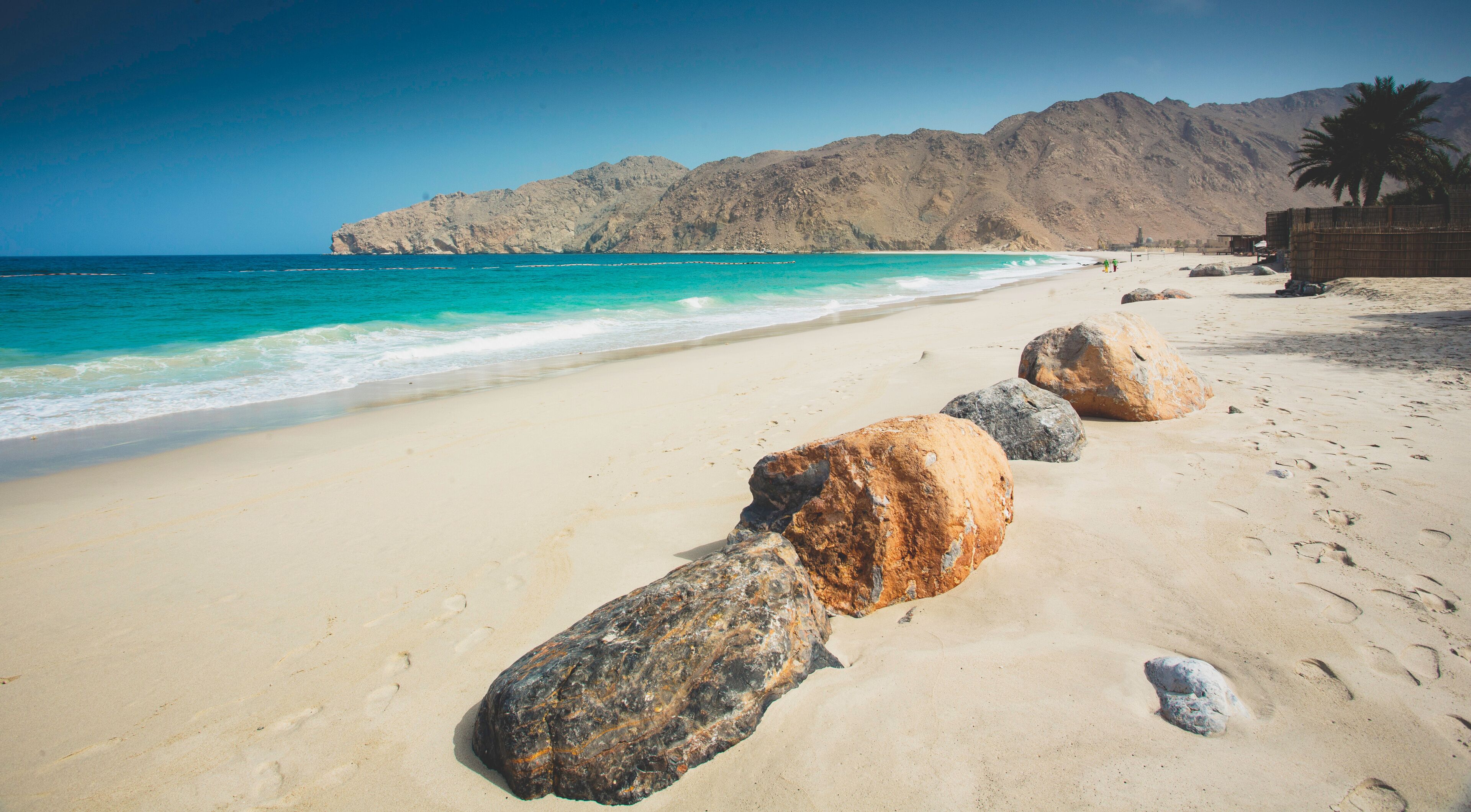 A sandy beach with large rocks in the foreground and a mountain range in the background.