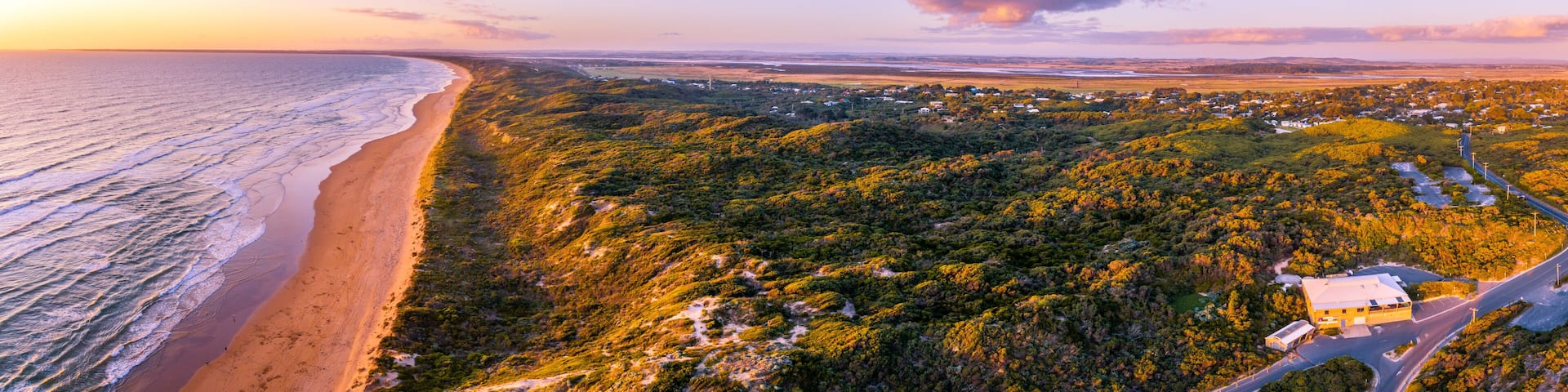 A coastal landscape with a beach, forested hills, and a small settlement.