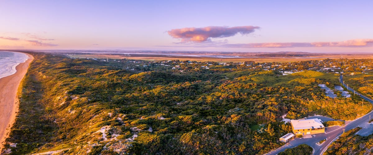 A coastal landscape with a beach, forested hills, and a small settlement.
