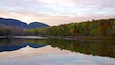 A calm lake reflecting autumn trees and mountains.