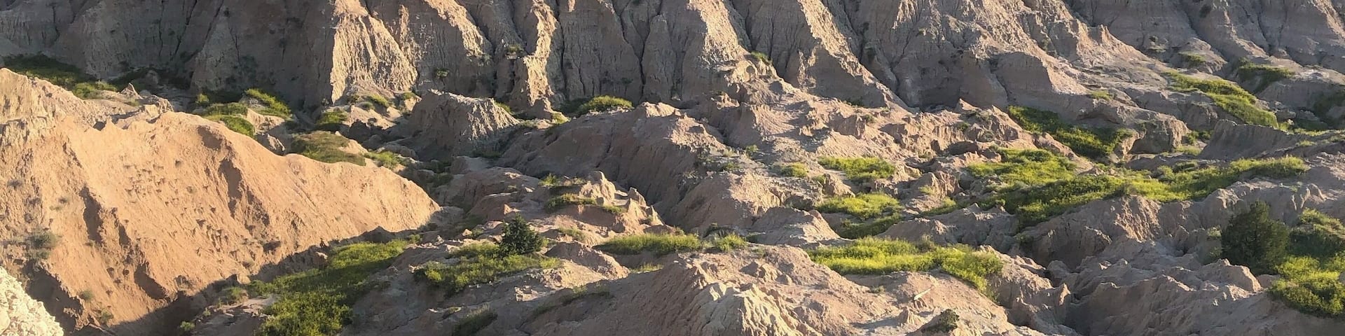 A vast landscape of rugged, eroded hills with patches of green vegetation.