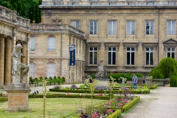 Un bâtiment historique à l’architecture classique, agrémenté d’une statue et doté d’un jardin bien entretenu.