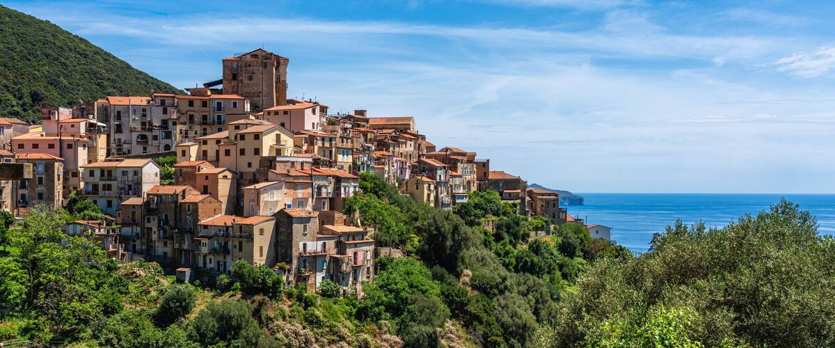 A coastal village with terracotta-roofed buildings nestled on a hillside, overlooking the sea.