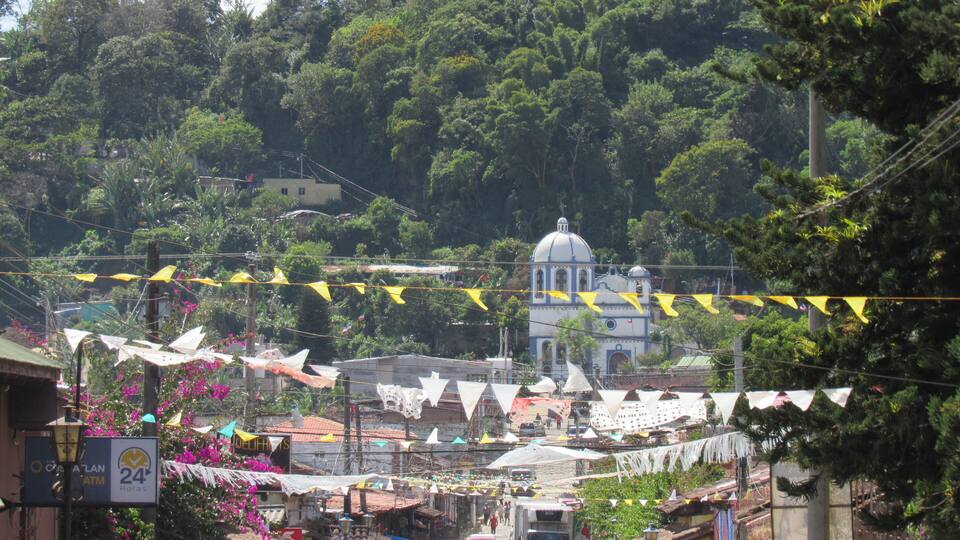 A bustling street with colorful flags, shops, and a church with a dome.
