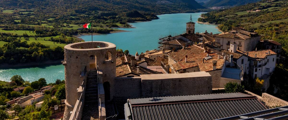 A mountainous landscape with a river, a tower, and a village with traditional architecture.