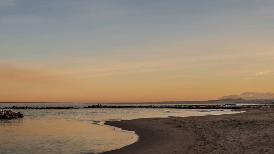 A beach with a rocky breakwater and a mountain in the background.