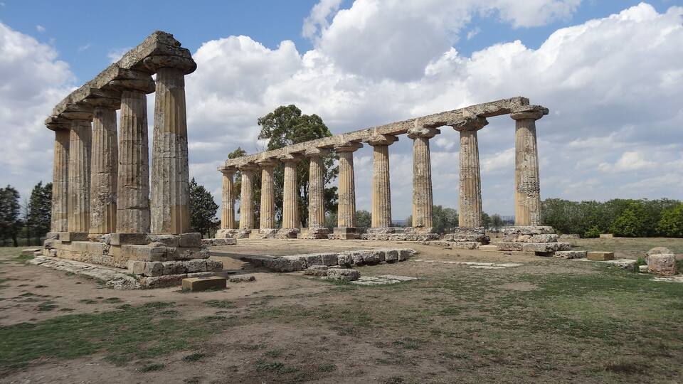 Ancient stone columns and ruins in a grassy field.