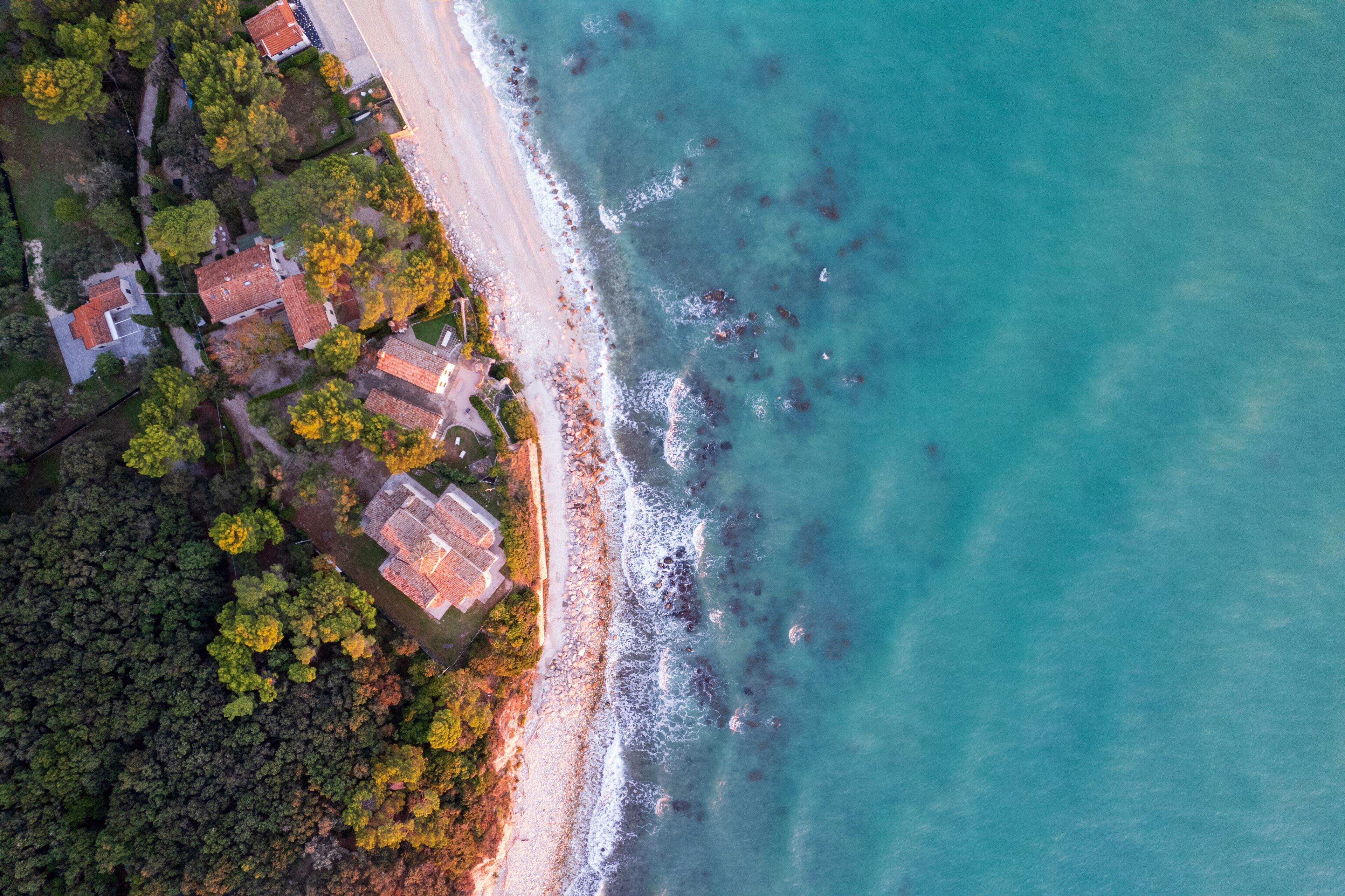 An aerial view of a coastal area with a beach, houses, and dense forest.