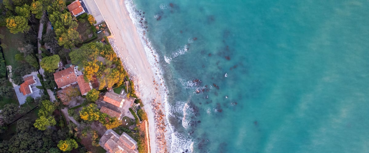 An aerial view of a coastal area with a beach, houses, and dense forest.