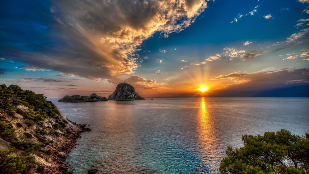 Un coucher de soleil sur un paysage côtier, avec des falaises rocheuses et une petite île.