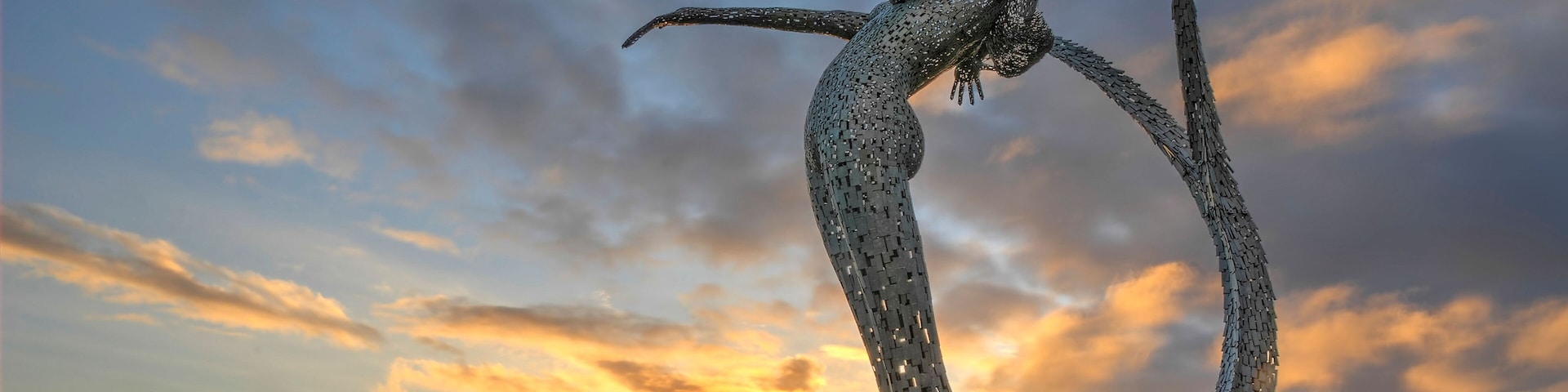 A sculpture of a woman in a dynamic pose, set against a sunset sky with clouds.