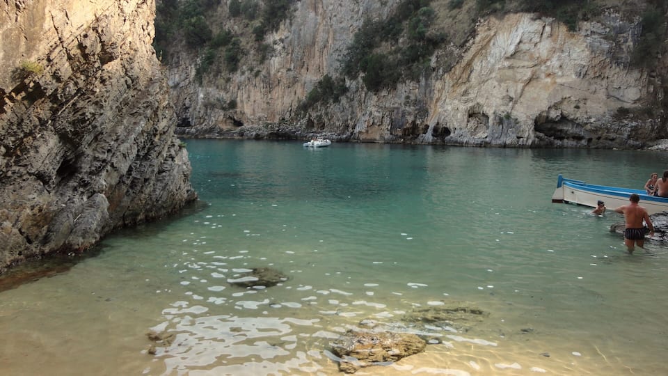A rocky canyon with clear turquoise water and a boat near the shore.