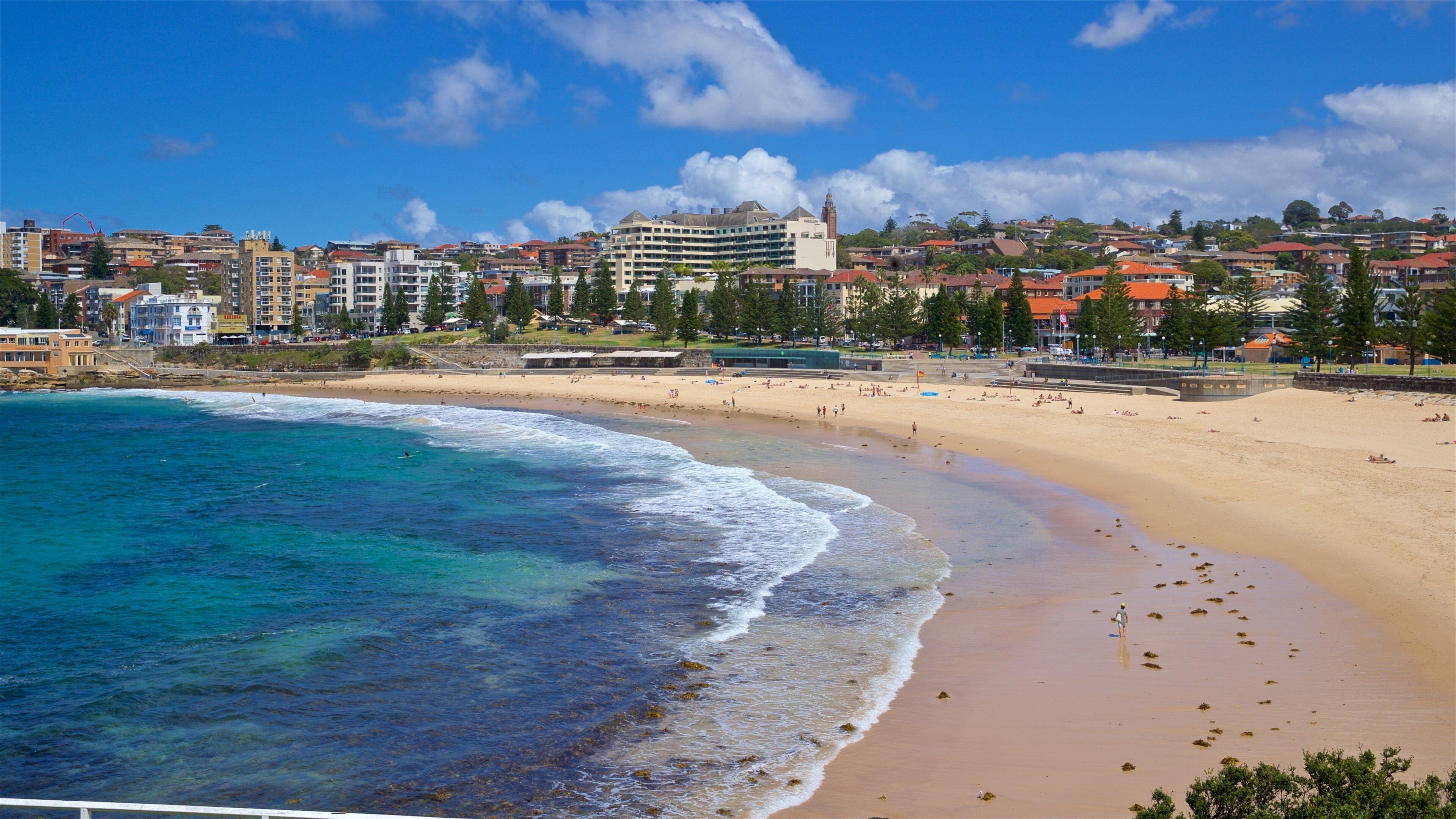 A coastal cityscape with a sandy beach, clear blue waters, and a prominent building with a clock tower.