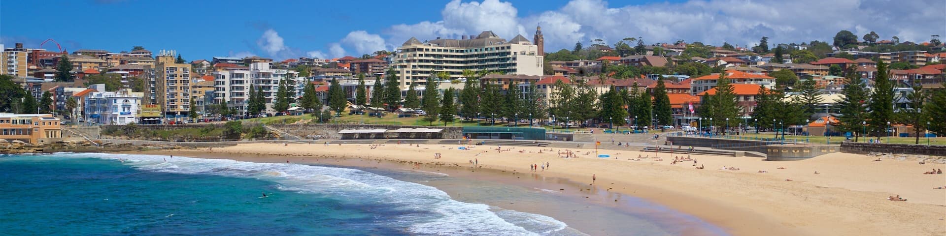 A coastal cityscape with a sandy beach, clear blue waters, and a prominent building with a clock tower.