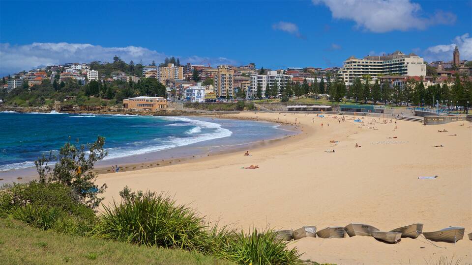A sandy beach with ocean waves, a cityscape in the background, and a clear blue sky.