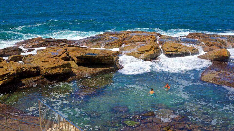 A rocky coastal area with clear water and two people swimming.