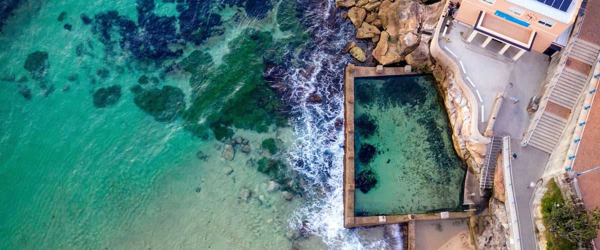 A coastal area with clear turquoise waters, a rocky shoreline, and a building with solar panels.