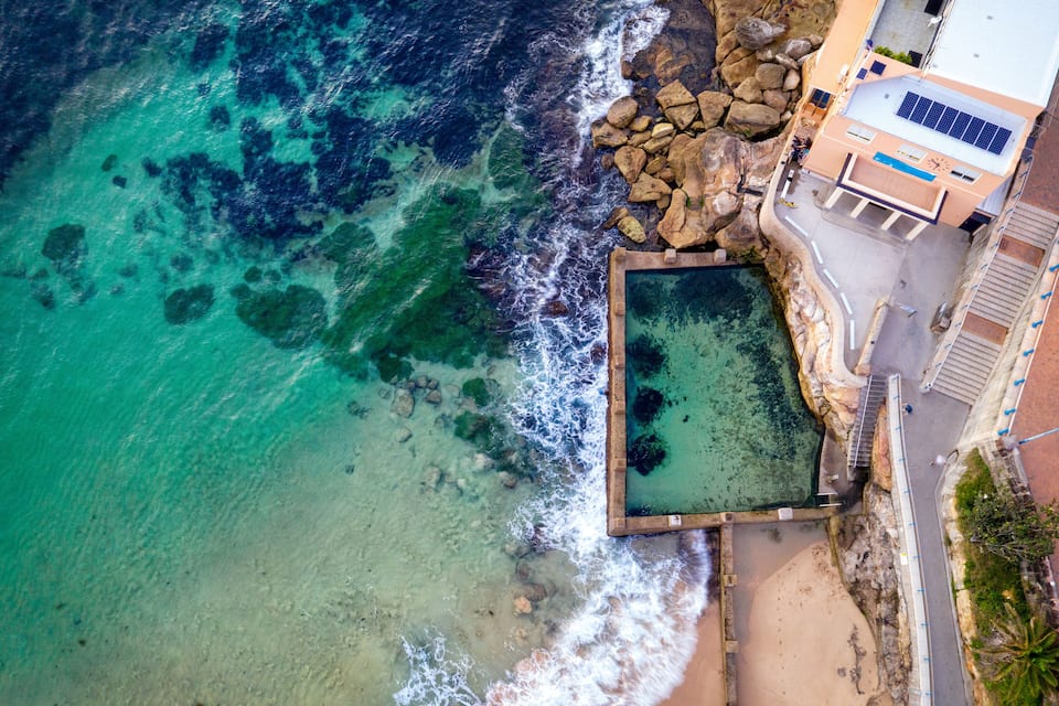 A coastal area with clear turquoise waters, a rocky shoreline, and a building with solar panels.