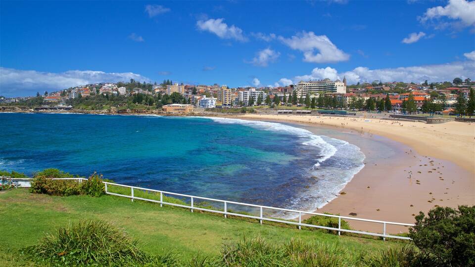 A coastal city with a sandy beach, clear blue waters, and a mix of residential and commercial buildings.