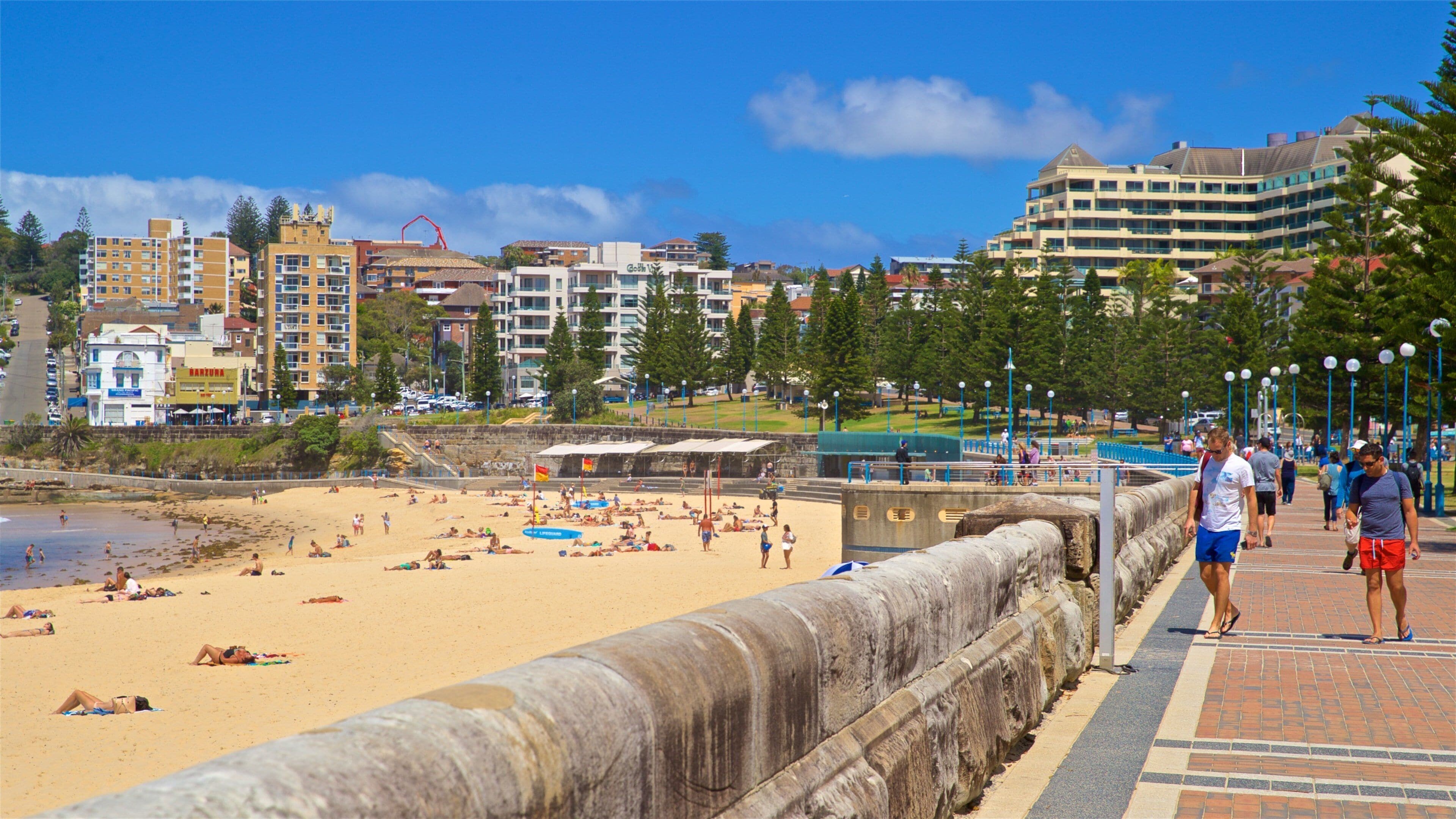 A beach with people sunbathing, a lifeguard tower, and buildings in the background.