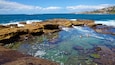 A rocky coastline with clear water and two people swimming.