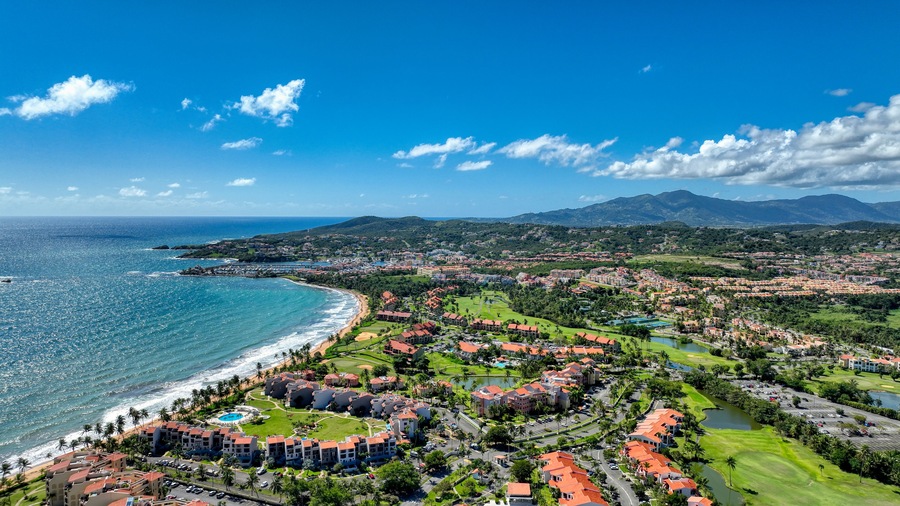 Western Aerial view of Palmas del Mar, Puerto Rico, A southern coast gated community with lush greenery, golf courses, coastline meeting the ocean and rolling hills.