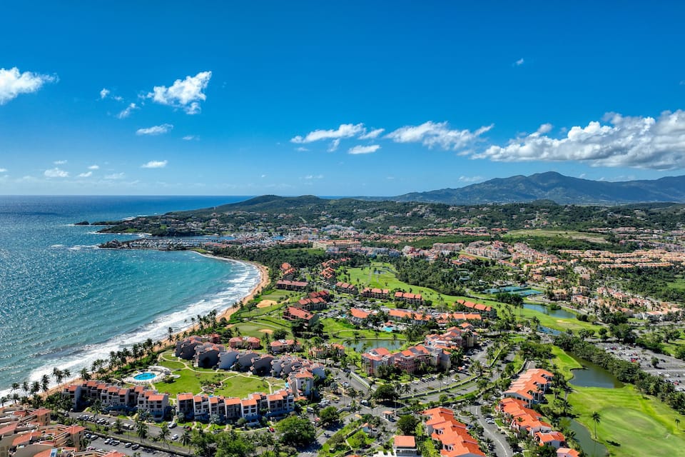 A coastal town with a beach, residential buildings, and mountains in the background.