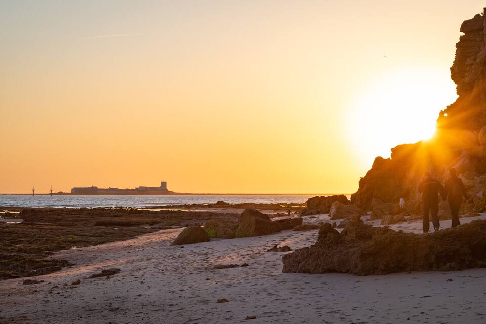 A rocky beach at sunset with the sun setting behind a cliff.