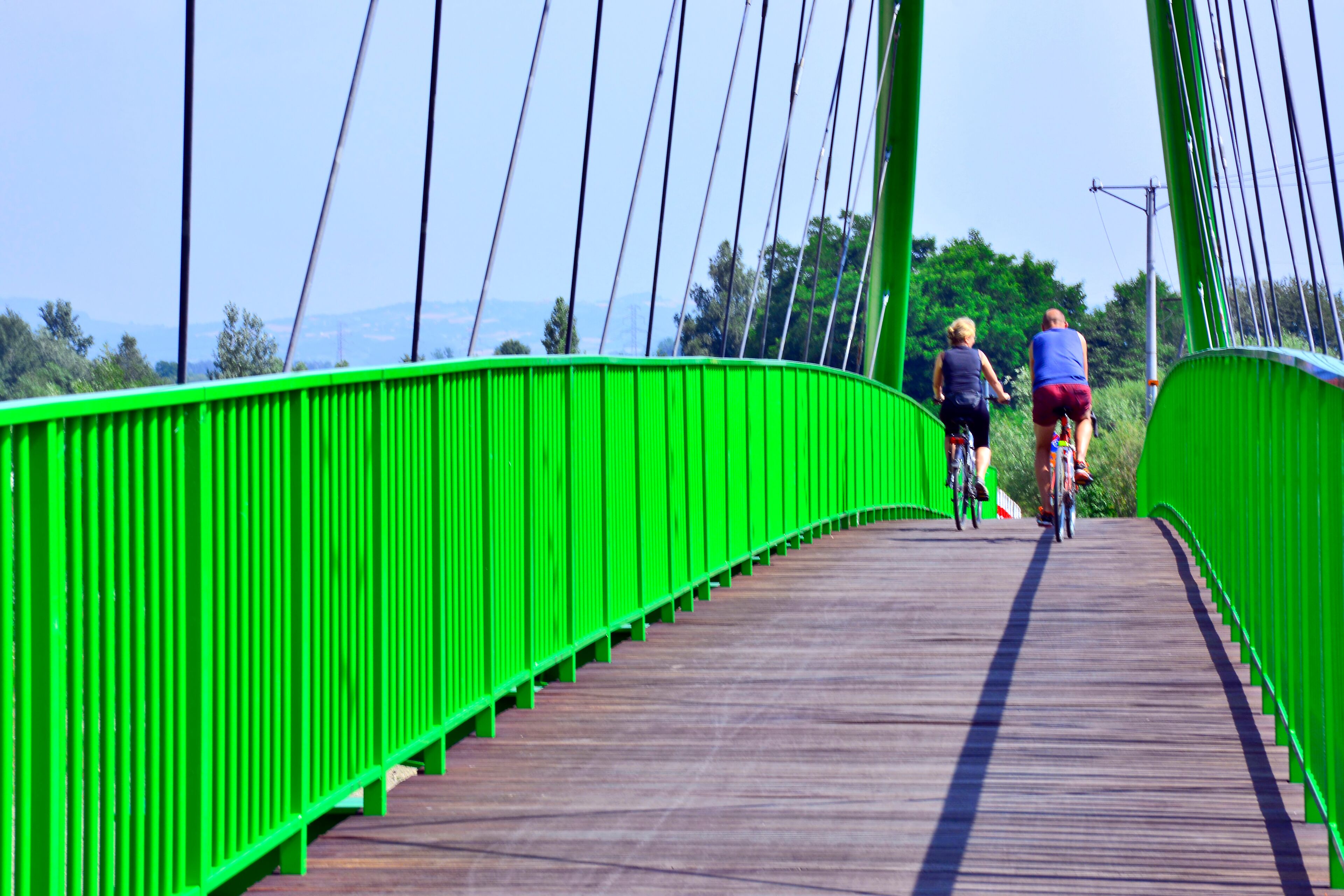 Two cyclists crossing the footbridge with green metal railing over the Poprad river  at Stary Sacz in Poland