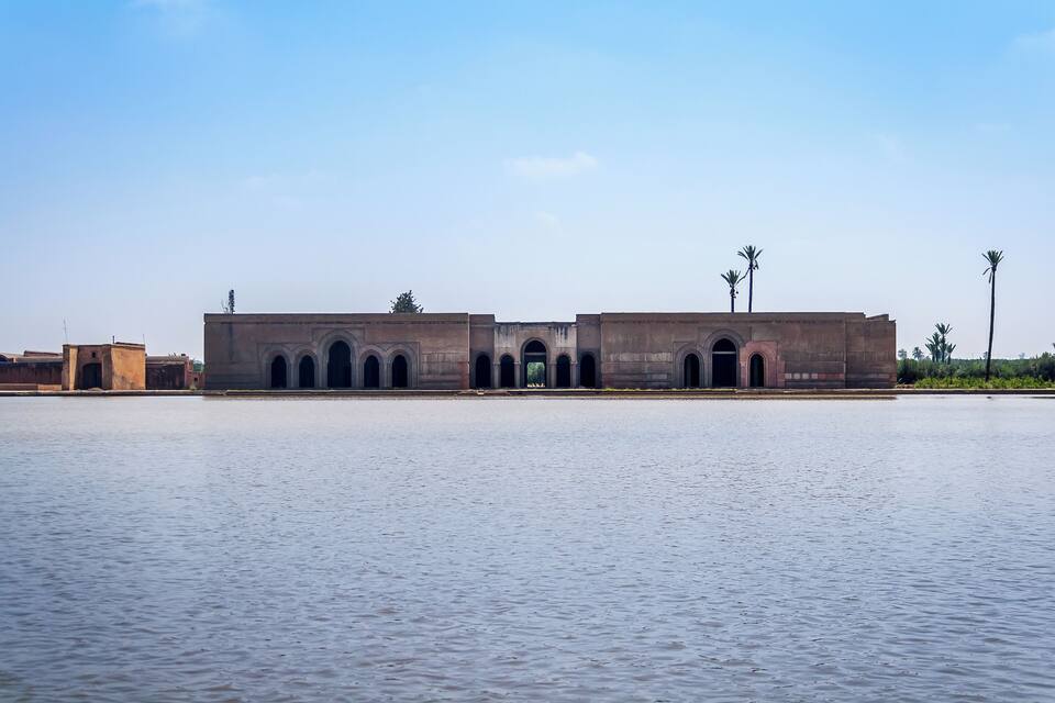 Un edificio grande y rectangular con múltiples arcos y un acceso central, ubicado junto a una masa de agua tranquila.