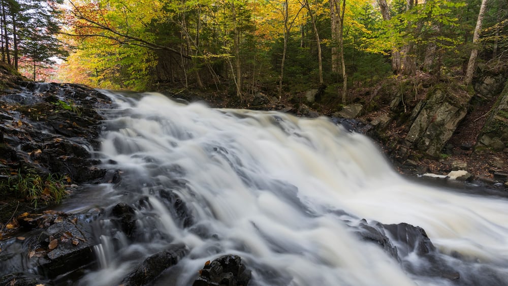 A waterfall cascading over rocks in a forested area with autumn foliage.