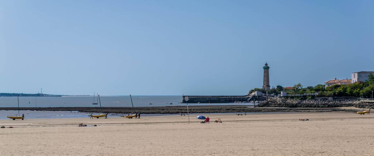 A sandy beach with yellow canoes, a lighthouse, and a rocky breakwater.
